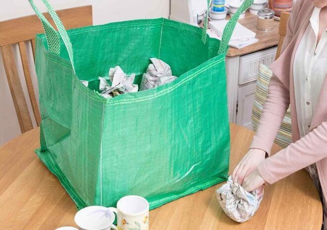 Women packing cups into a green storage and moving bag.