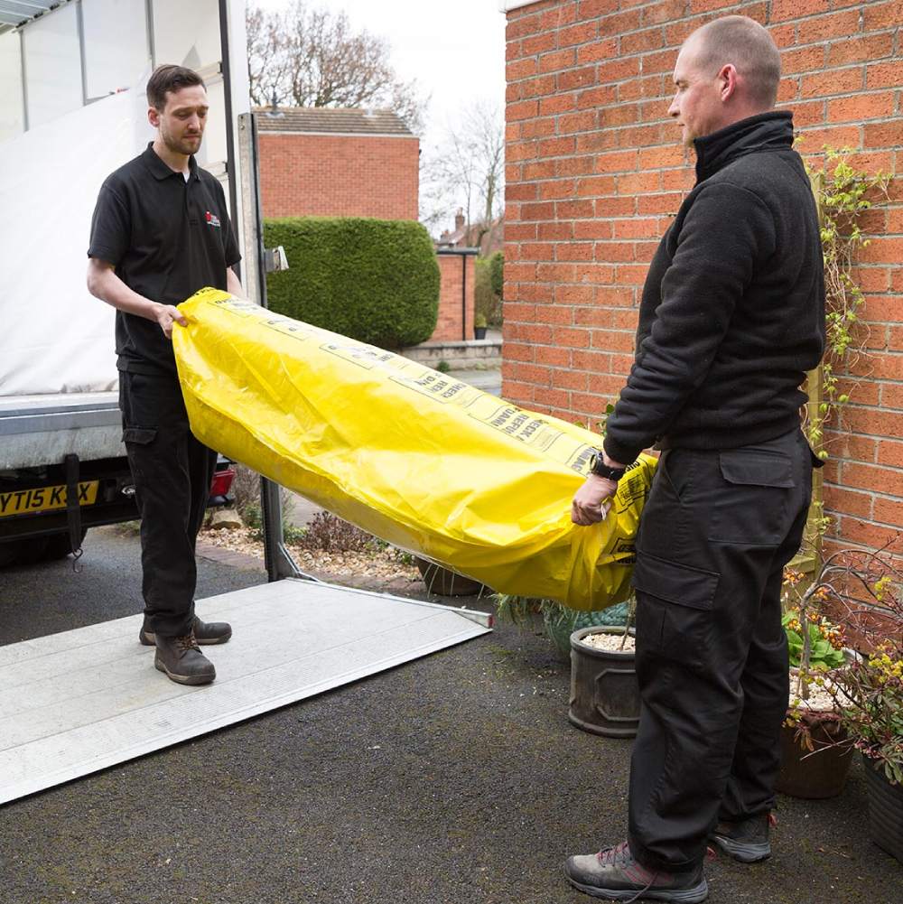 Removals men lifting a rug which is protected inside a reusable carpet and rug bag
