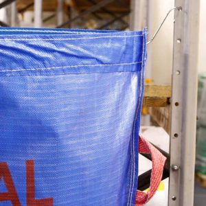 Waste sack hanging on warehouse racking with hooks and eyelets.